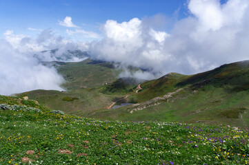 Fototapeta premium Green summer mountains, beautiful hills covered in green grass. Big fluffy clouds, or fog, over the mountains. Hiking season.