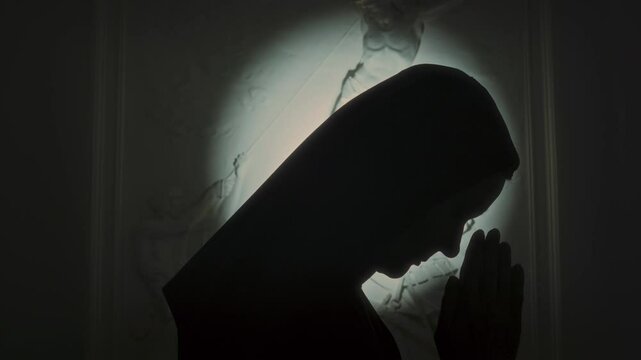 Side view of silhouette of nun in monastic hood praying to Lord, low key backlighting
