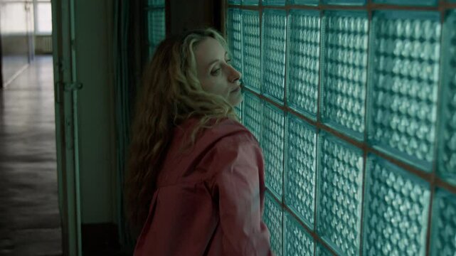 Young inspired woman with long blonde hair performing dance improvisation by glass block wall in hallway