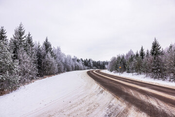 Beautiful view of winding road through snowy forest with frost-covered trees under overcast sky. Sweden.