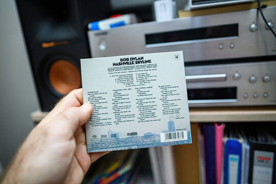Paris, France - Mar 18, 2024: POV of a male hand holding a Bob Dylan SACD Nashville Skyline while reading the rear part of the disc with the song list, with audiophile hi-fi devices s
