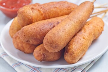 Heap of corn dogs on white plate, served with ketchup, horizontal