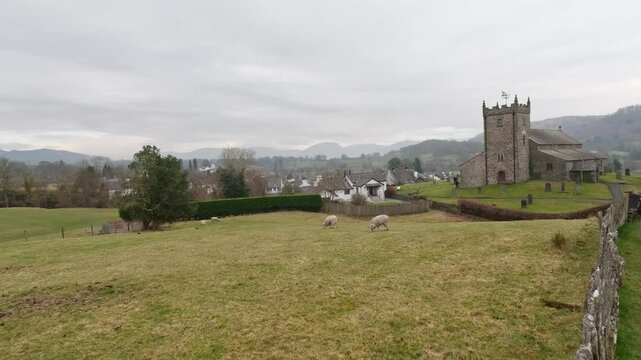 St Michael & All Angels Church in Hawkshead, showing fields and grazing sheep Cumbria,