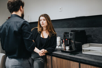 In a contemporary office kitchen, a male and female colleague engage in a relaxed conversation during a coffee break, emphasizing a friendly workplace environment.