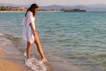 Fototapeta premium Beautiful woman on the sea shore touching the water with her foot.