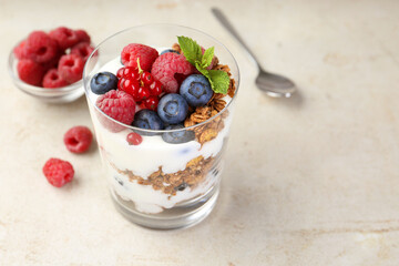 Tasty yogurt with fresh berries, granola and mint in glass on gray textured table, closeup. Space for text