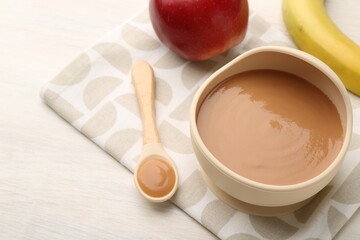 Delicious baby food in bowl and ingredients on white wooden table