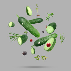 Ripe cucumbers, herbs and spices falling on grey background