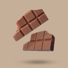 Pieces of sweet chocolate falling on beige background