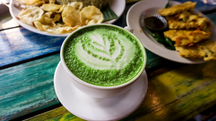 A cup of matcha latte with indonesian food in the background