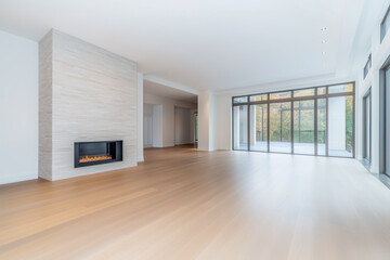 Obraz premium Bright and spacious modern living room featuring a sleek fireplace, large floor-to-ceiling windows, and light wooden flooring, offering an open and airy atmosphere