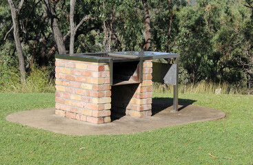 Fototapeta premium Outdoor brick barbecue grill in a park surrounded by grass and trees