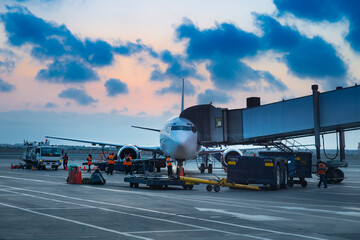 A large white airplane is parked on the tarmac with several people working on it