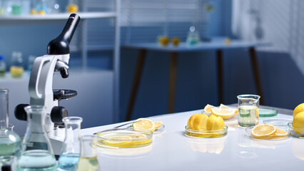 Plenty of fresh yellow lemons placed in a petri dish on laboratory background with many lab glassware in white flat form. Laboratory photo for advertising or testing lemon products.