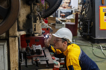 Male mechanical or metallic engineer is using a torch light to check a welding machine for maintenance and quality control. Expert is inspecting or repairing an automatic machine in a metallic factory