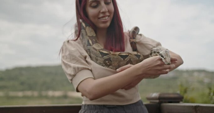 A woman with red hair smiles with a large snake around her shoulders.