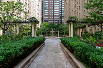 This elegant urban courtyard in New York City features meticulously landscaped gardens surrounded by classic brick buildings. The lush greenery and peaceful setting create a serene retreat amidst the 