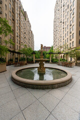 Obraz premium A beautifully designed urban courtyard nestled between historic brick buildings in New York City. This tranquil space boasts lush, manicured gardens, providing a peaceful escape from the city's hustle