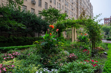 This elegant urban courtyard in New York City features meticulously landscaped gardens surrounded by classic brick buildings. The lush greenery and peaceful setting create a serene retreat amidst the 