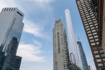 Fototapeta premium This striking New York City photo captures the contrast between towering modern skyscrapers and historic brick buildings, all viewed from a rooftop perspective. The image highlights the architectural 