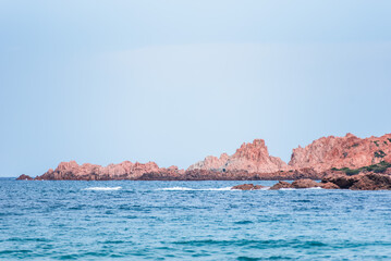 From the shores of Isola Rossa, the vibrant blue waters of the bay meet the striking pink rocks and lush green hills of the coastline. 