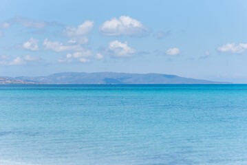 Fototapeta premium Le Saline beach landscape: turquoise sea meets a distant horizon with faint landforms, under a vast blue sky. A breathtaking view capturing the serene beauty of Sardinia's coastline.