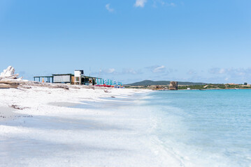 Le Saline beach landscape: turquoise sea meets a distant horizon with faint landforms, under a vast blue sky. A breathtaking view capturing the serene beauty of Sardinia's coastline.