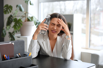 Obraz premium Young woman with bottle of water suffering from headache sitting in office