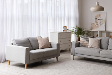 Cozy sofas near large window with transparent curtains in living room