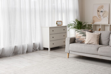 Cozy sofa and chest of drawers near large window in living room