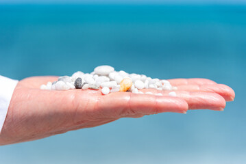 An open hand cradles the essence of the shore, tiny pebbles resting gently, a quiet offering to the vast, blurred sea in the background—symbolizing a connection between the earth and the infinite.