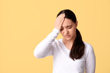 Beautiful young woman suffering from headache on yellow background