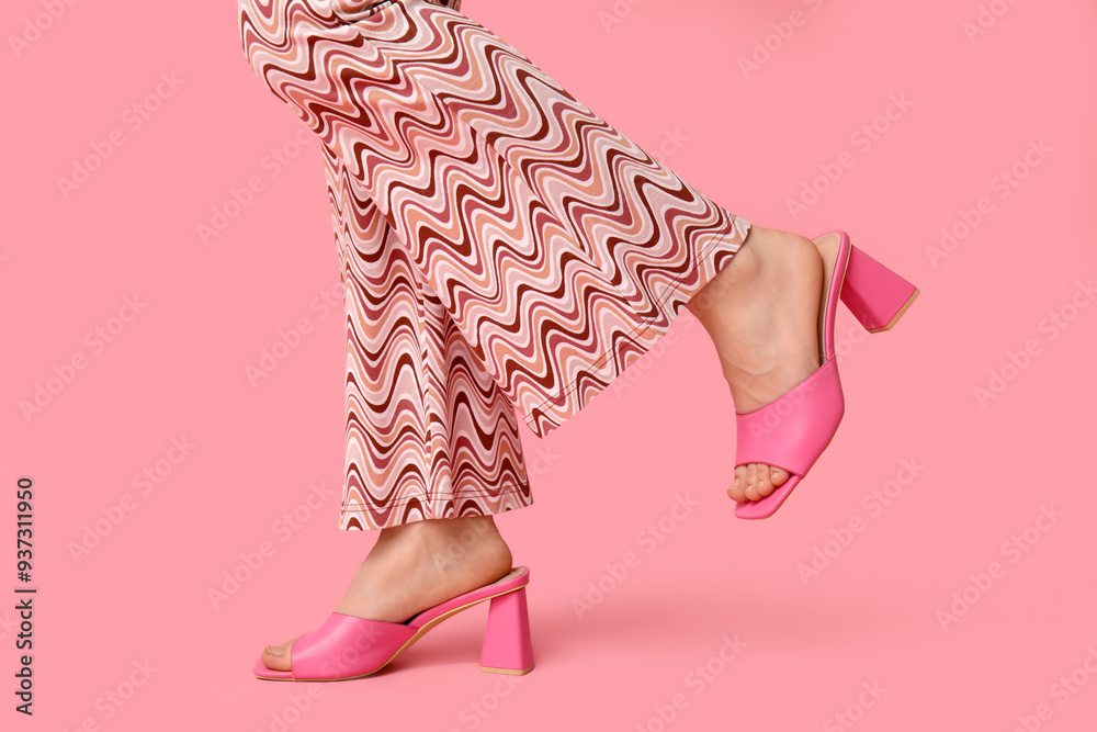 Sticker Legs of young woman in trousers and pink open-toed high heels on pink background