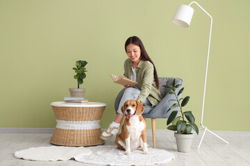 Young woman reading book on armchair near adorable Beagle dog in living room