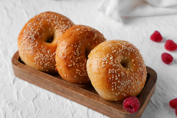 Wooden board with tasty bagels and raspberries on white background