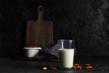 Glass of fresh almond milk and nuts on black background