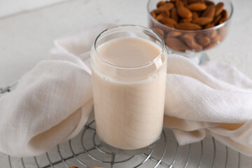Glass of fresh almond milk and bowl with nuts on white background