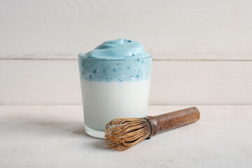 Glass of blue dalgona matcha latte and chasen of milk on grunge table