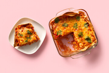 Baking dish and plate with tasty enchilada on pink background