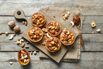 Tasty tarts with nuts and caramel sauce on board against brown wooden background
