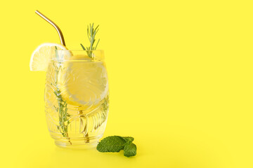 Glass of fresh lemonade with rosemary and mint on yellow background