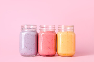 Mason jars of different fresh smoothie on pink background