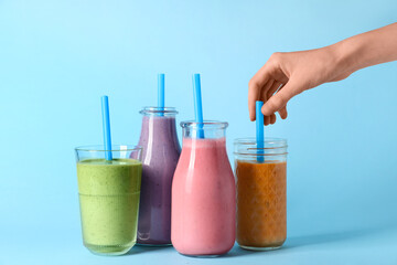 Female hand with glasses and bottles of different fresh smoothie on blue background