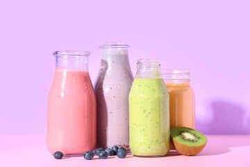 Bottles of different fresh smoothie with kiwi and blueberries on lilac background