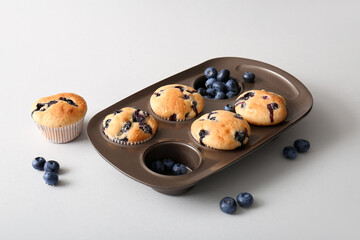 Baking tray with tasty blueberry muffins on white background