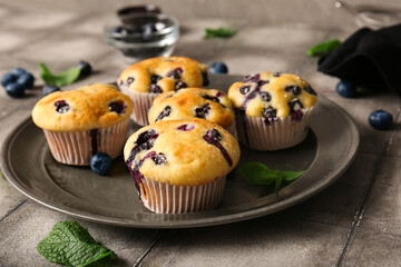 Plate with tasty blueberry muffins on grunge tile background, closeup