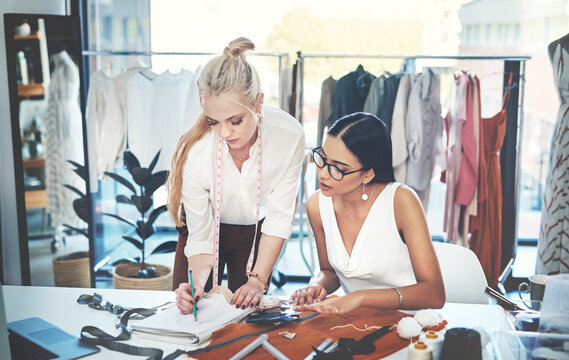 Woman, fashion and designers with book at workshop for writing, material or design at office. Young, female person or team of tailors taking notes on garment for size, style or clothing production
