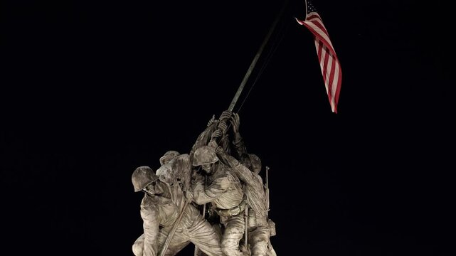 A slow upward tilt of the World War 2 Memorial showing soldiers planting the USA flag against a night sky in Washington D.C.
