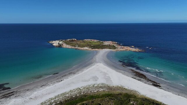 Drone approaching shot of Diamond Island surrounded by blue turquoise water in summer. Sandy path connecting island. Bicheno city, Tasmania. Wide shot.