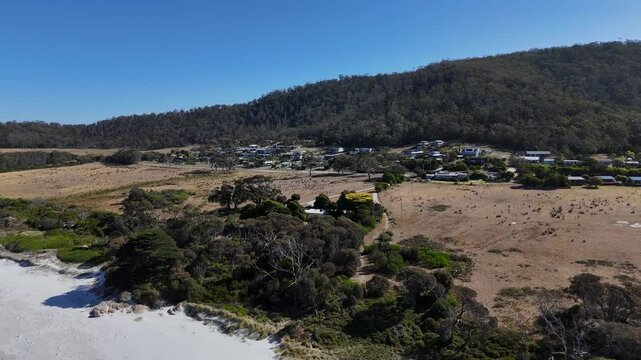 Aerial view of small Bicheno Town in Tasmania during sunny day in summer. Sandy beach and fields in foreground. Wide shot.